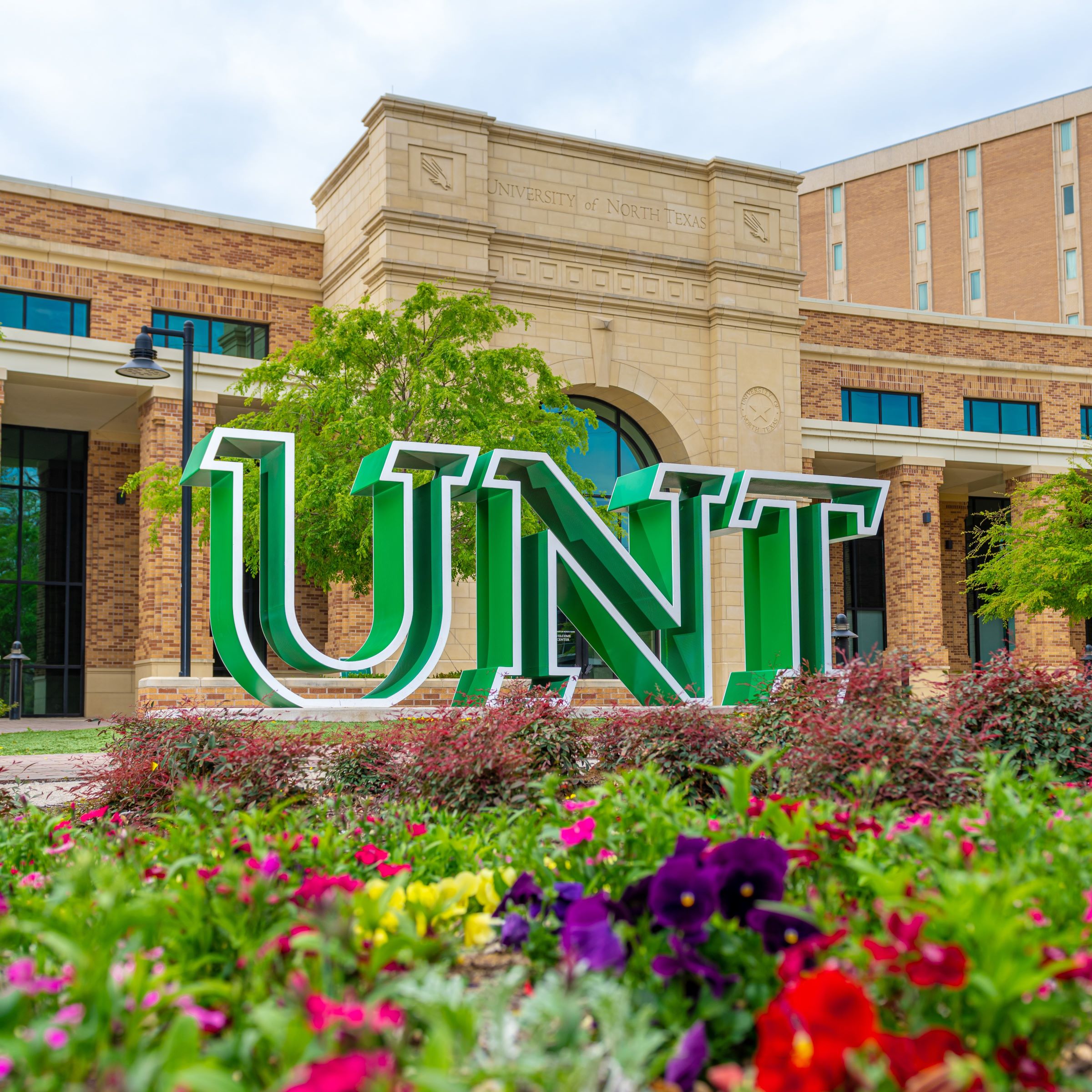 Green and white U-N-T letters outside the Welcome Center. Flowers are in the foreground.