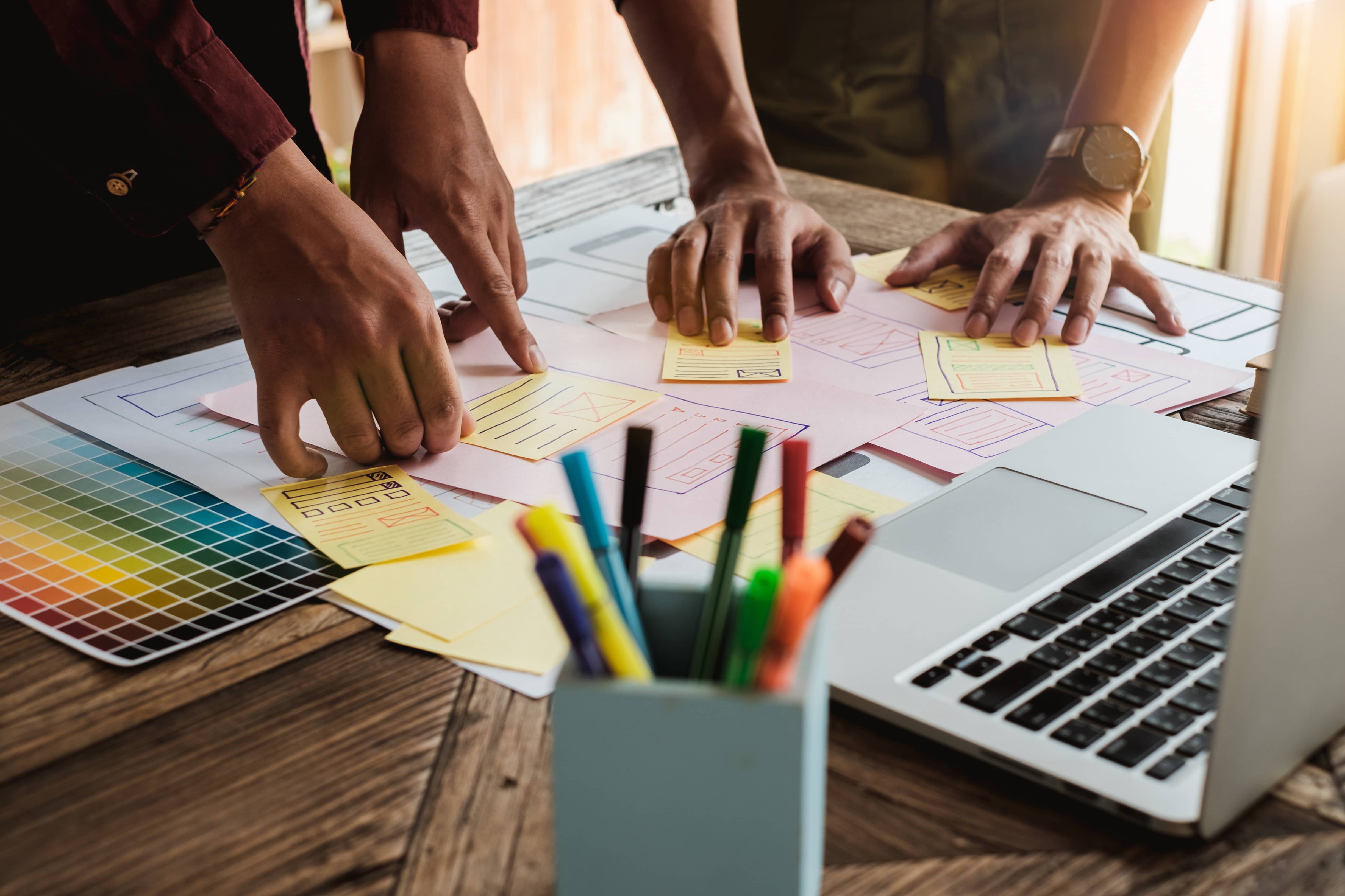 two people collaborating on a desk with a laptop and colorful pens